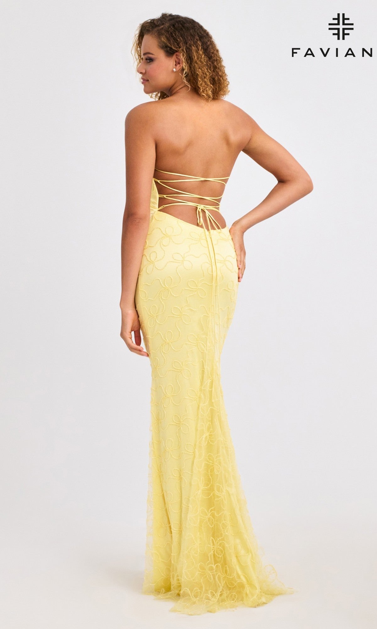 A woman wears the Faviana 11416 long yellow beaded prom dress, featuring lace-up strappy open back details, as she stands facing away from the camera against a plain white background with the